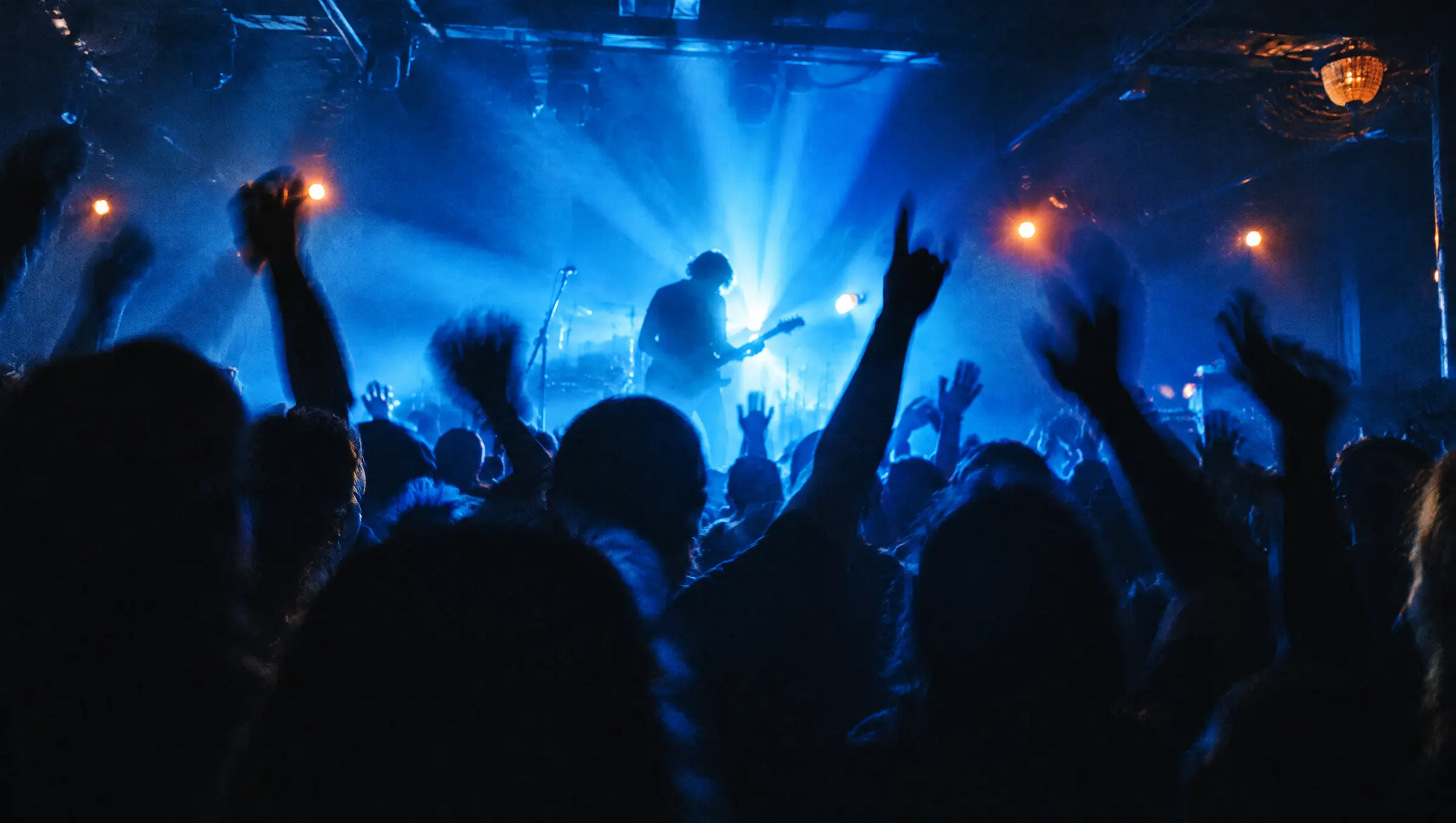 A crowd with raised hands in front of a backlit stage