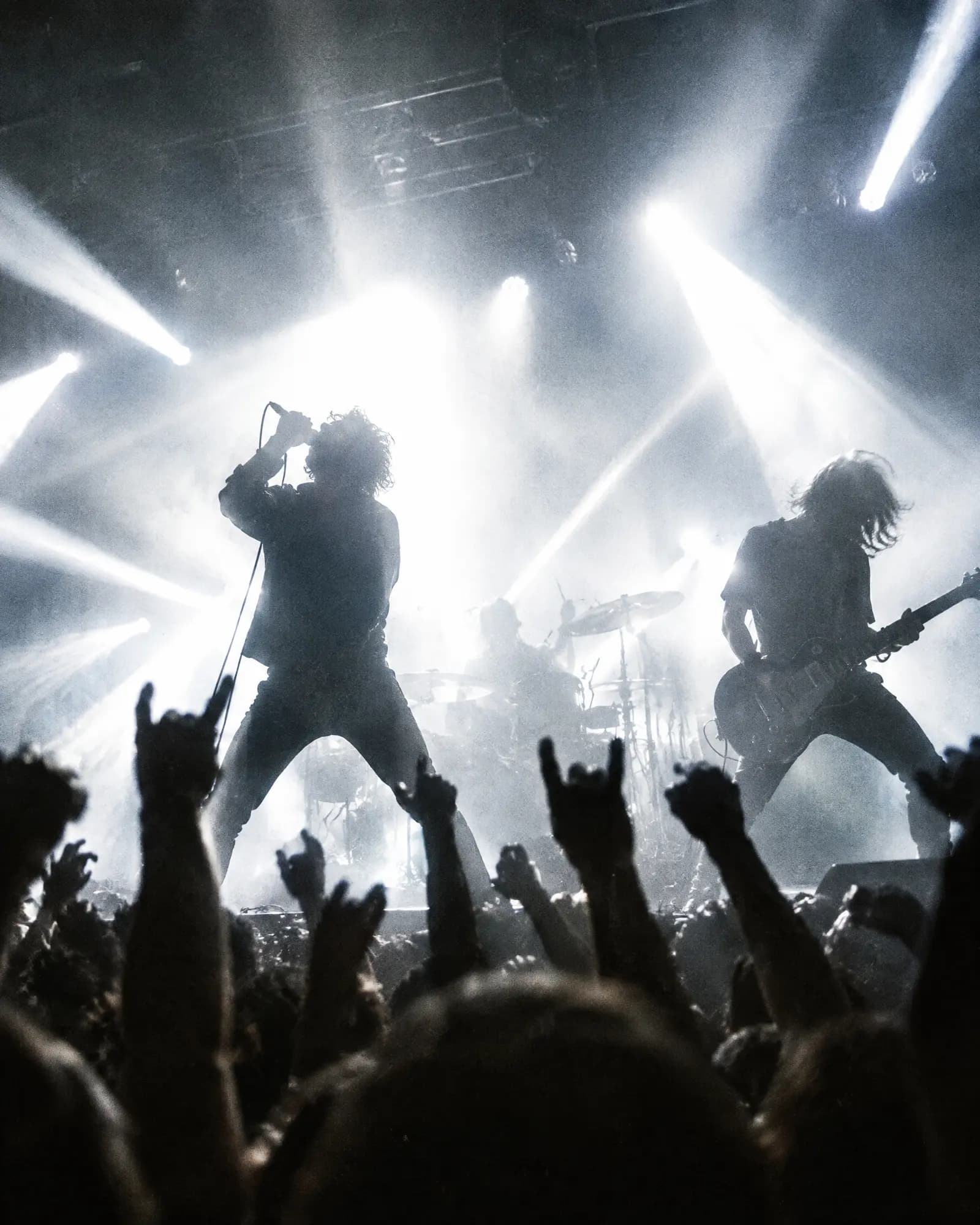 A rock band backlit by white stage lights, hands raised in the front row