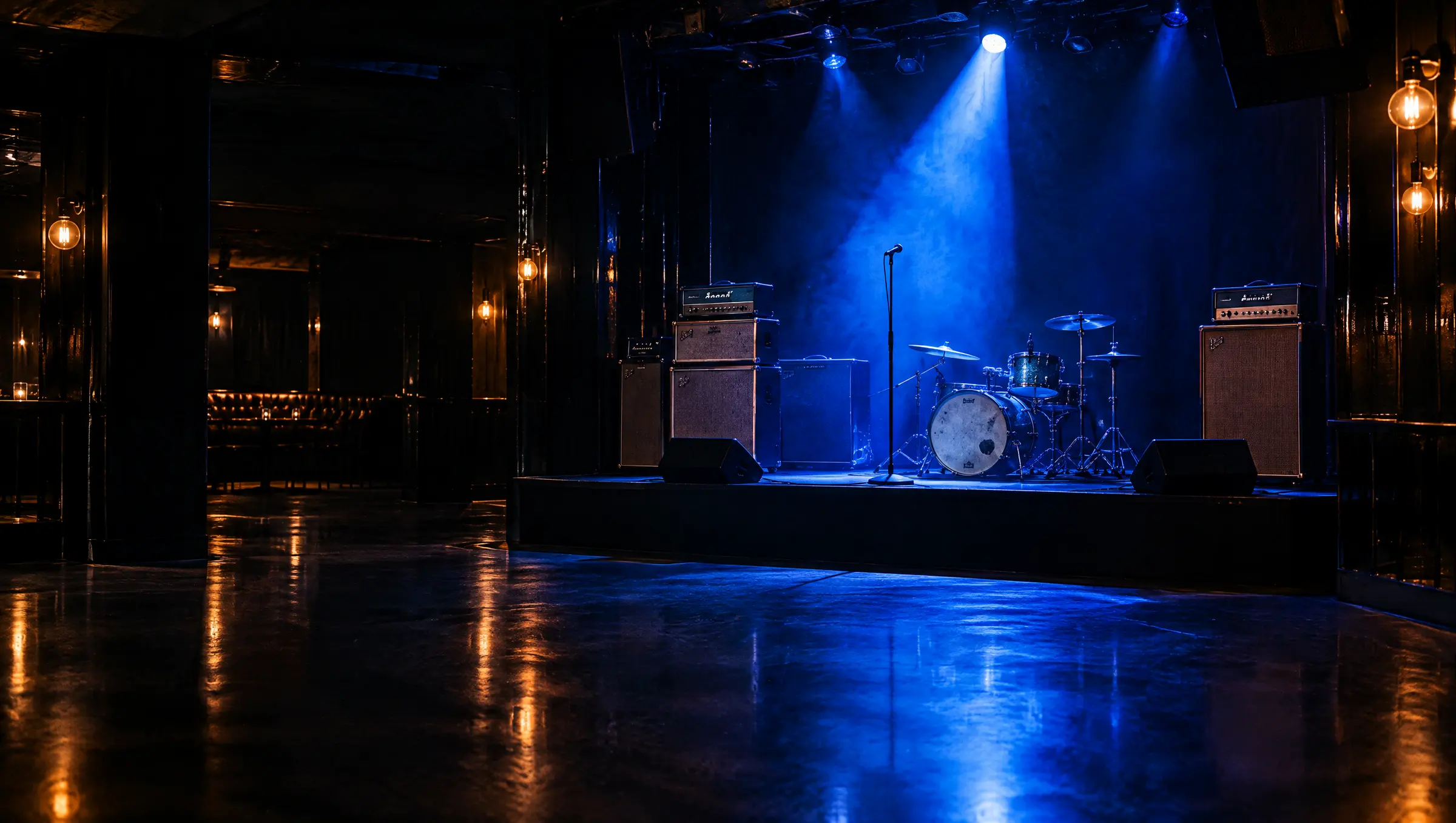 An empty club stage with amplifiers and a microphone in a cobalt spotlight